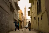 Une ruelle étroite avec des bâtiments colorés, des jeunes joueurs de foot et un minaret en arrière-plan.