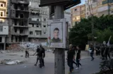 Une affiche d'un jeune homme souriant sur un poteau, avec un bâtiment en ruine en arrière-plan.