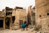 Des bâtiments en ruines, avec des graffiti, deux personnes se tiennent devant.