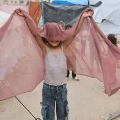 Bambino felice che salta con un velo rosato, in un ambiente di tende.