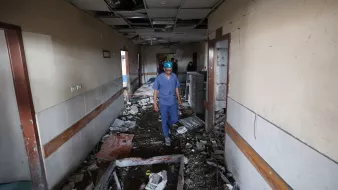 Couloir d'un bâtiment endommagé, débris partout, homme en tenue de protection avance prudemment.