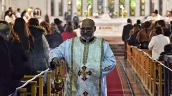 Un prêtre en tenue liturgique, portant un encensoir, dans une église pleine de fidèles.