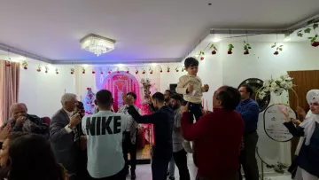 فضای شاد، مردم در حال رقص، تزئینات گل و نورپردازی رنگارنگ، یک کودک در آغوش بزرگترها.