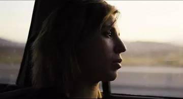 L'image montre une silhouette d'une personne assise à l'intérieur d'une voiture. Elle regarde par la fenêtre, prenant un moment de réflexion. La lumière est douce, créant une ambiance mélancolique, et le paysage flou en arrière-plan suggère un voyage en cours. Le visage de la personne est partiellement éclairé, mettant en valeur une expression pensante.
