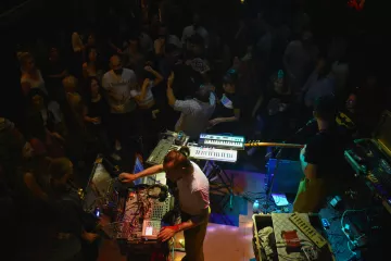 A lively concert scene with musicians using electronic instruments, surrounded by an energetic crowd.