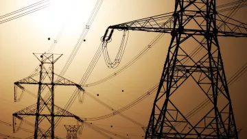 Silhouettes de pylônes électriques contre un ciel orangé.