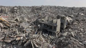 L'immagine mostra un vasto paesaggio di distruzione, con edifici in rovina e detriti sparsi ovunque. Ci sono strutture crollate e macerie che si estendono fino all'orizzonte, creando un'atmosfera di desolazione e abbandono.