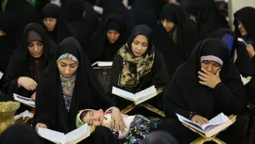 در تصویر گروهی از زنان با چادرهای سیاه در حال مطالعه قرآن دیده می‌شوند. بعضی از آن‌ها در حال خواندن هستند و توجه عمیقی به کتاب دارند. همچنین، یک کودک در آغوش یکی از زنان خوابیده است. به‌طور کلی، فضایی معنوی و پر از تمرکز در این تصویر وجود دارد.