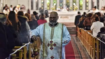 Un prêtre en tenue liturgique, portant un encensoir, dans une église pleine de fidèles.