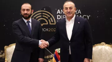 L'image montre deux hommes se serrant la main, probablement en signe de coopération ou de négociation. Ils sont vêtus de costumes formels. L'arrière-plan présente le logo d'un événement lié à la diplomatie, avec la mention "Ankara Diplomacy 2023". L'ambiance semble être celle d'une rencontre officielle.