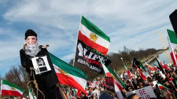 L'image montre une grande manifestation, probablement en faveur de la liberté ou des droits de l'homme. Au premier plan, une marionnette représentant un homme âgé est portée par un manifestant, tandis que d'autres personnes tiennent des drapeaux iraniens et des pancartes. Les participants semblent unis et déterminés, exprimant leurs revendications. L'ambiance est dynamique, avec une foule nombreuse et des symboles visuels forts liés à leur cause.