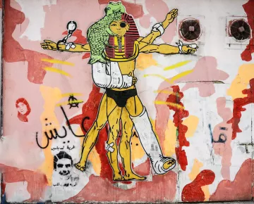 L'image représente une fresque murale colorée, incluant des éléments graphiques variés. Au centre, une figure humanoïde est stylisée avec des références à la culture égyptienne, incorporant des motifs inspirés des pharaons. Cette figure a plusieurs bras, symbolisant peut-être la force ou la multiplicités des rôles. Le fond est composé de formes abstraites et de couleurs vives, comme le rouge et le jaune, créant un contraste avec le personnage principal. On peut également apercevoir des inscriptions en arabe. L'ensemble véhicule une esthétique urbaine et contemporaine.