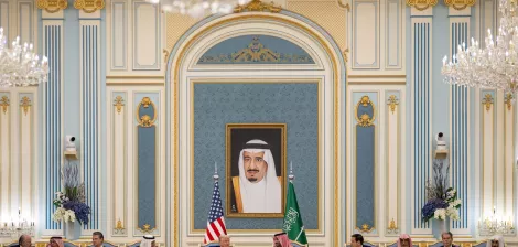 A formal meeting with leaders seated in an ornate room, a large portrait on the wall.