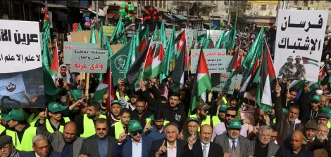 A large crowd marches, holding Palestinian flags and banners, in a show of solidarity.